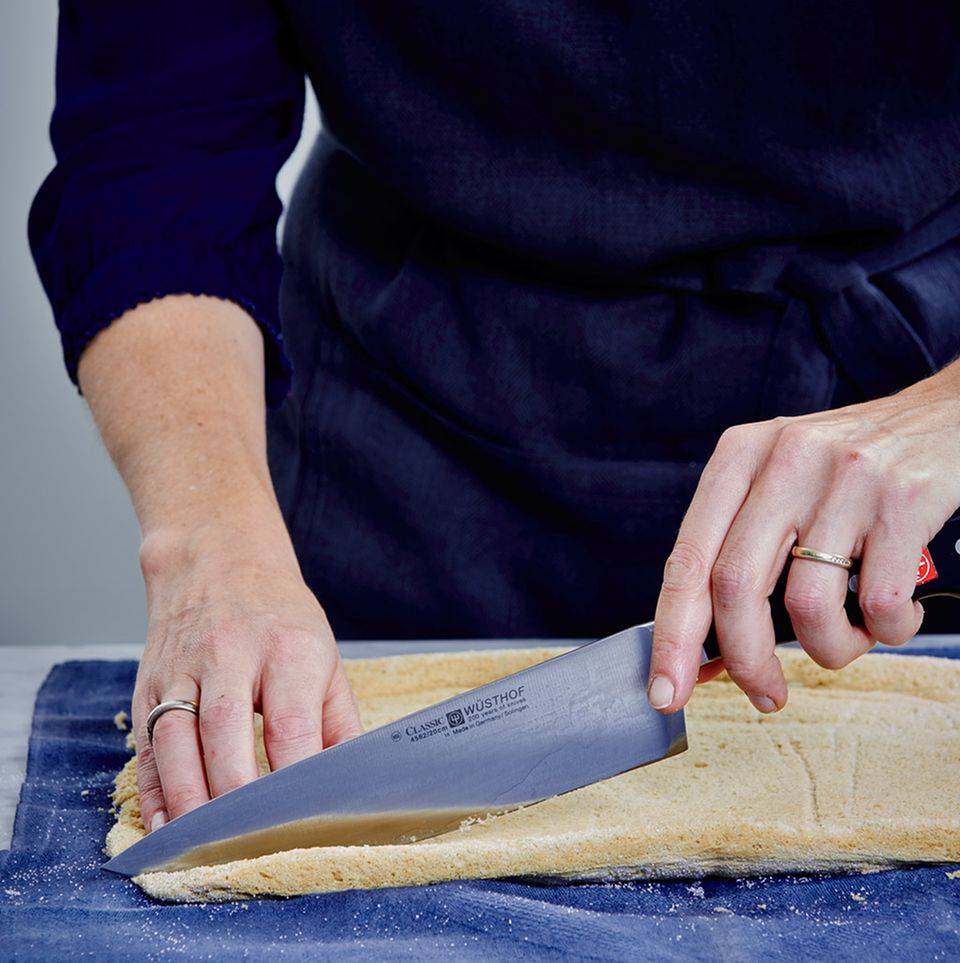Biskuit auf dem Küchentuch mit einem Messer zuschneiden Biskuit auf dem Küchentuch mit einem Messer zuschneiden