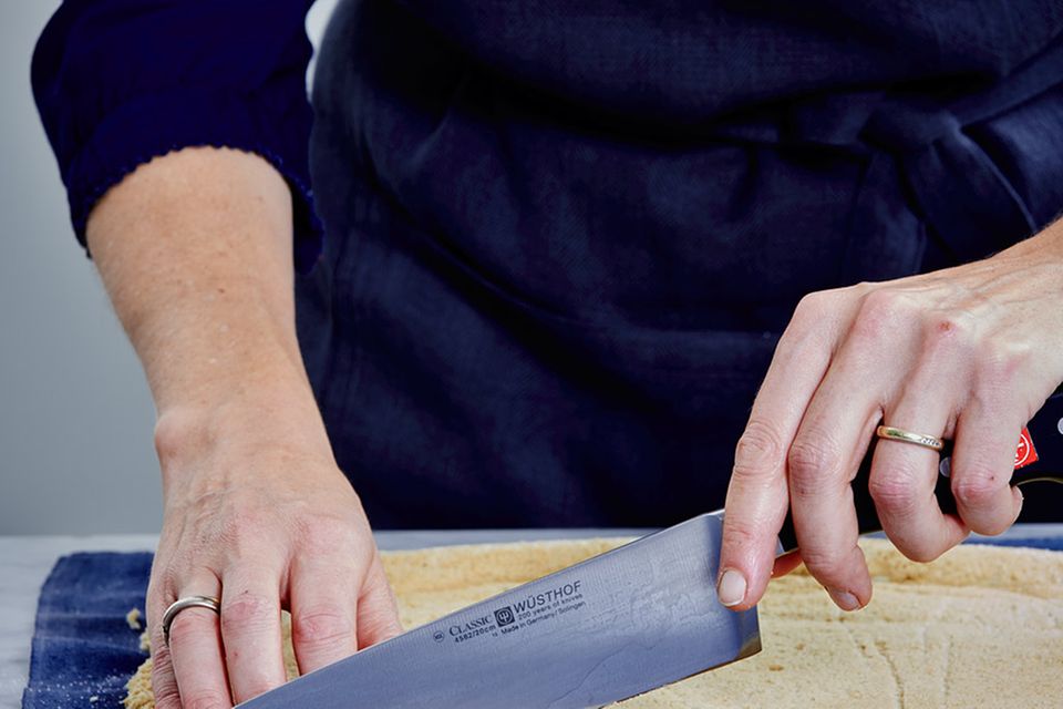 Biskuit auf dem Küchentuch mit einem Messer zuschneiden
