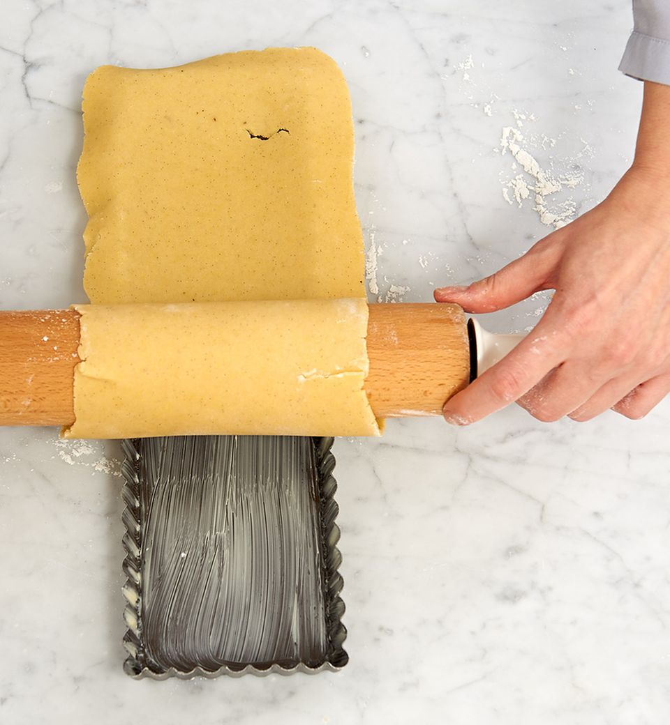 Um das Rollholz gewickelt lässt sich der Teig ganz einfach in die Tarteform legen Um das Rollholz gewickelt lässt sich der Teig ganz einfach in die Tarteform legen