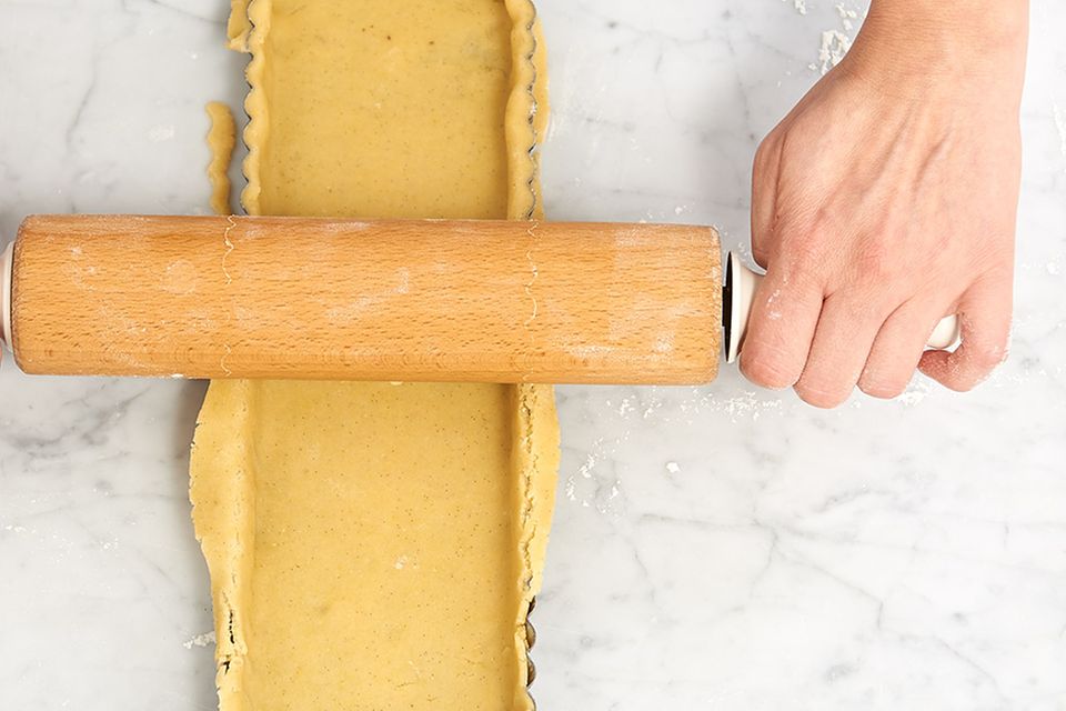 Teig in der Tarteform mit dem Rollholz begradigen