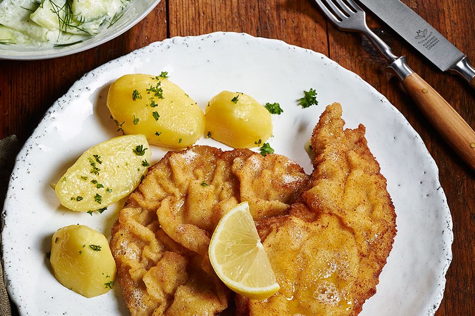 Wiener Schnitzel serviert mit Petersilienkartoffeln, Gurkensalat und Zitronenspalten