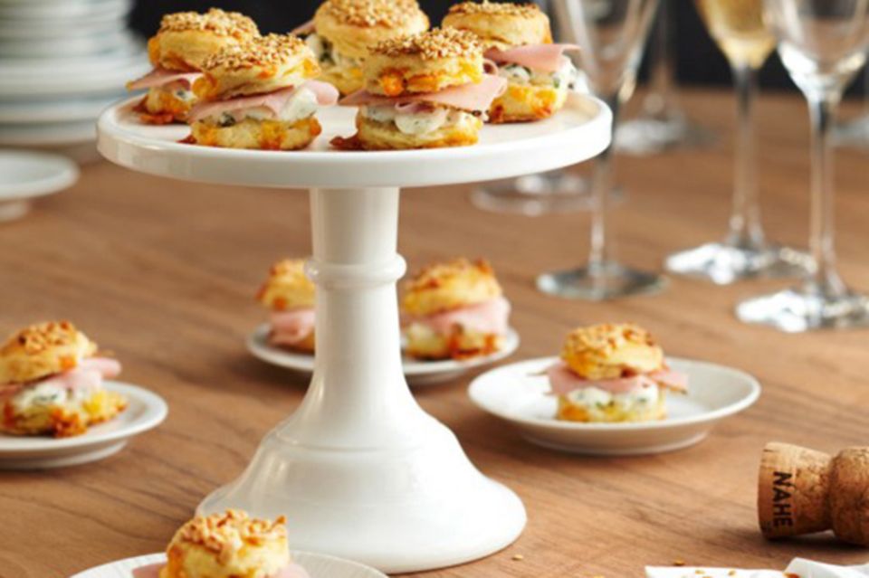 Kleine Cheddar-Scones mit Kräutercreme angerichtet auf einer Tortenplatte Kleine Cheddar-Scones mit Kräutercreme angerichtet auf einer Tortenplatte