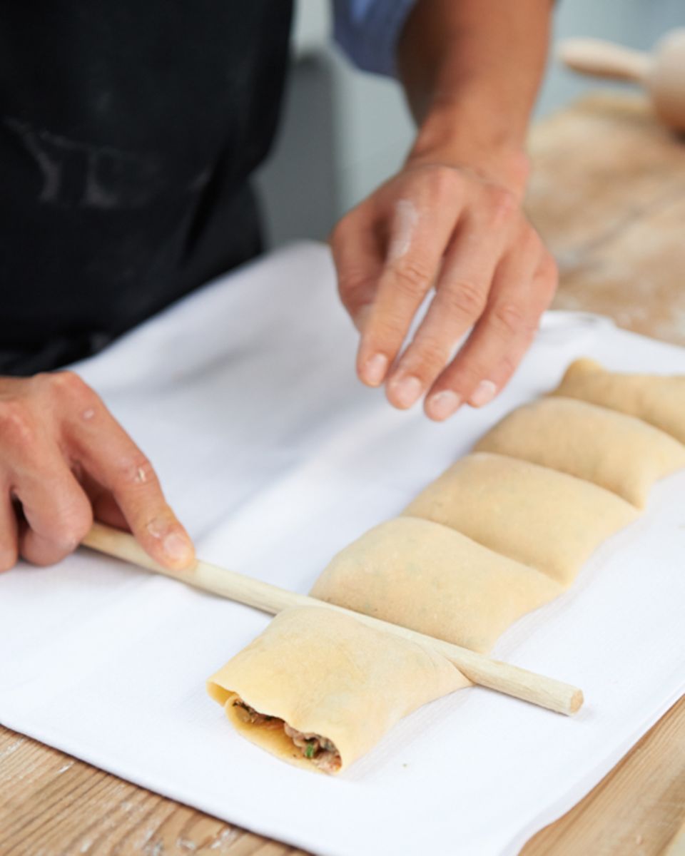 Die Maultaschenrolle mithilfe eines Kochlöffelstiels unterteilen Die Maultaschenrolle mithilfe eines Kochlöffelstiels unterteilen