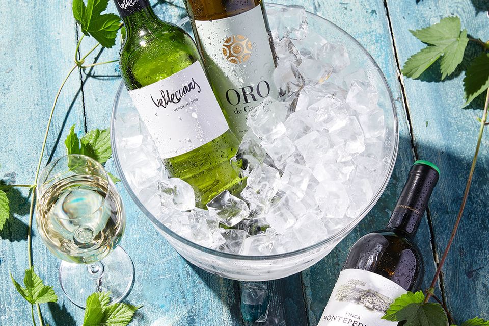 Weißwein Verdejo in Flaschen in einem Kühler mit Eiswürfeln und Weißwein im Glas