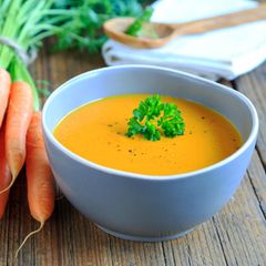 Karottensuppe im Teller und Karotten daneben