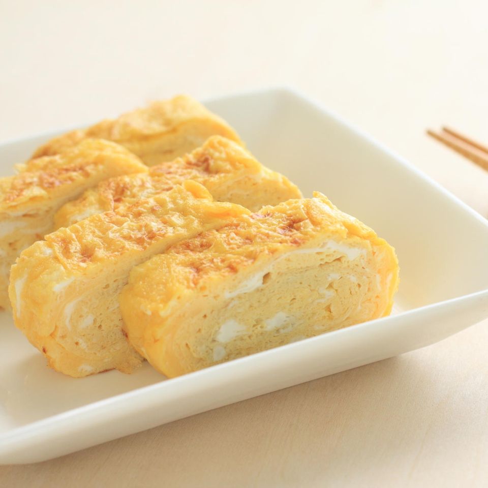 Tamagoyaki - Japanisches Omelett auf weißem Teller mit Essstäbchen an der Seite.