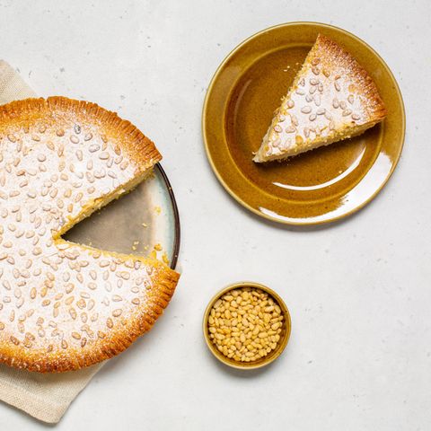 Angeschnittener Kuchen Torta della nonna, ein Kuchenstück auf einem Teller und eine Schale mit Pinienkernen