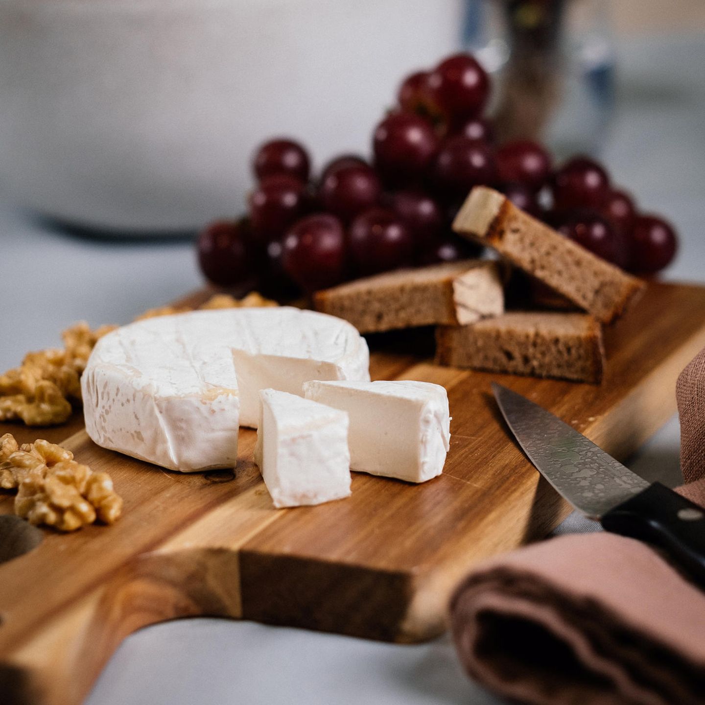 Soft White Camembert Style von Mondarella aufgeschnitten auf Holzbrett mit Brot und Trauben