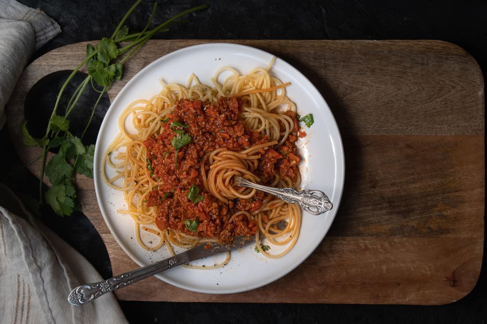 Vegane Spaghetti Bolognese auf weißem Teller auf Holzbrett
