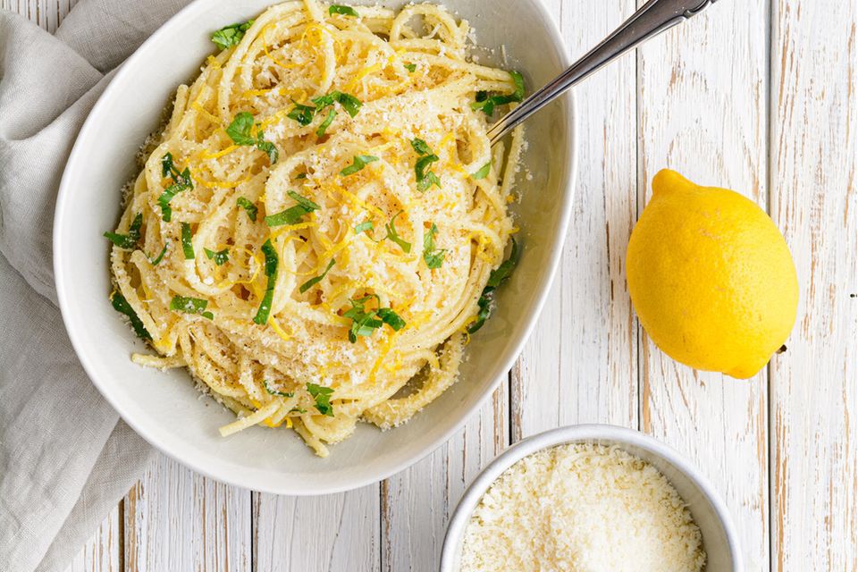Weiße, ovale Schale mit Spaghetti neben Zitronen und einer Schale mit Parmesan.