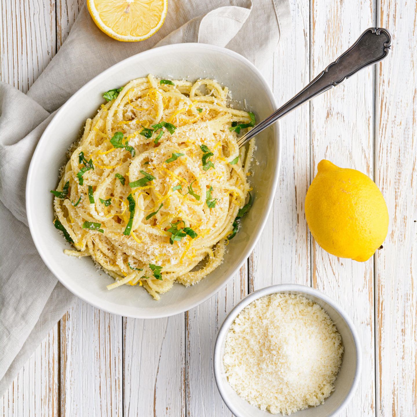 Weiße, ovale Schale mit Spaghetti neben Zitronen und einer Schale mit Parmesan.