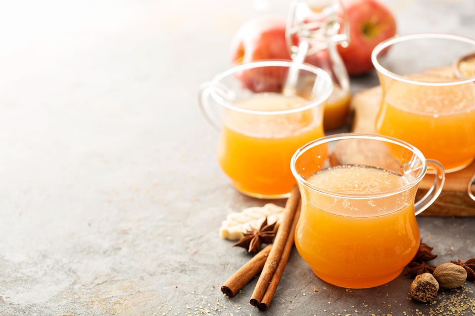 Apfelpunsch in Glasbecher mit Zimtstange, Sternanis und Keksen im Hintergrund