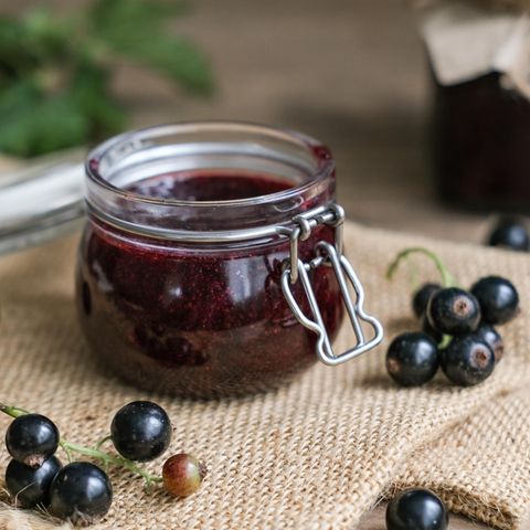 Dunkles Johannisbeergelee aus schwarzen Johannisbeeren im Glas neben einigen frischen Johannisbeerrispen auf Sackleinen