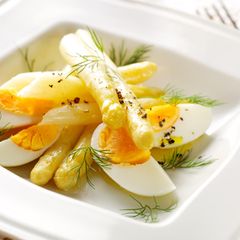 Weißer Spargel mit geviertelten Eiern auf einem weißen Teller mit Vinaigrette und Dill serviert.