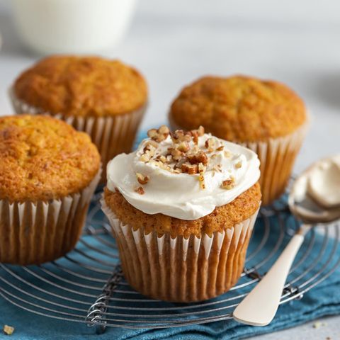 Möhren-Muffins in Muffinförmchen, teils ohne, teils mit Frischkäse-Frosting und gehackten Nüssen auf einem Kuchengitter