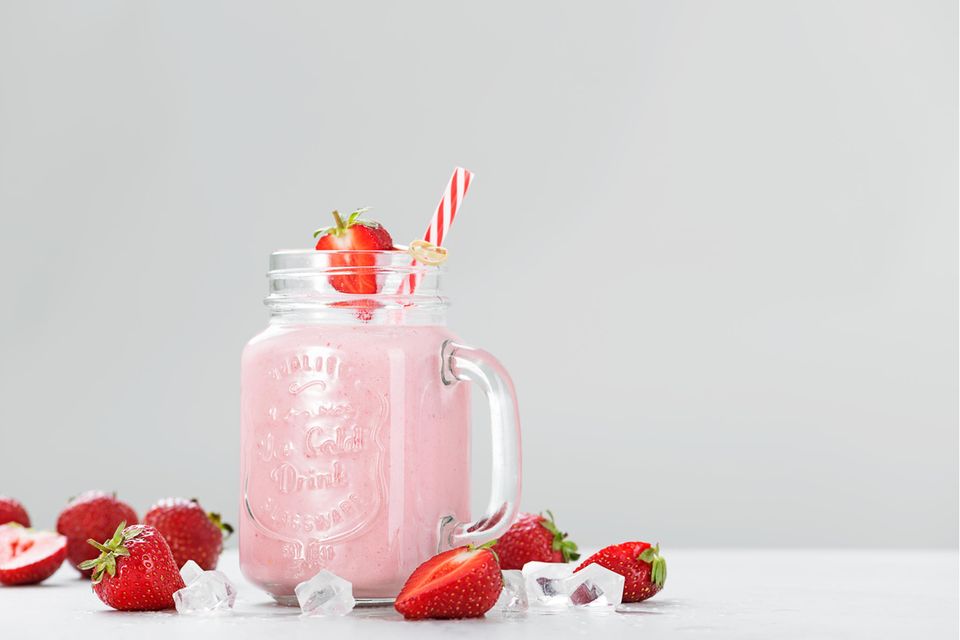 Erdbeer-Milchshake in Henkelglas mit Strohalm auf weißem Grund mit Erdbeeren und Eiswürfeln zur Deko