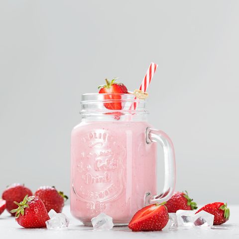 Erdbeer-Milchshake in Henkelglas mit Strohalm auf weißem Grund mit Erdbeeren und Eiswürfeln zur Deko