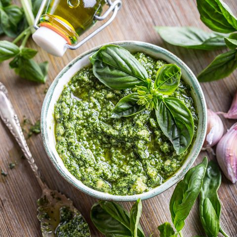 veganes Pesto in kleiner Porzellanschale auf Holztisch mit Basilikum und Olivenöl
