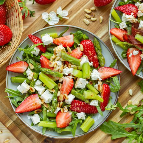 Spargelsalat mit Erdbeeren, Rucola, Feta und Pinienkernen auf hellblauem Teller