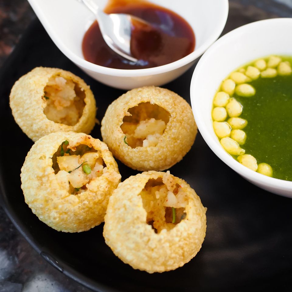 Indische Pani Puri als ballonförmige kleine Snacks mit Kartoffel-Kichererbsen-Füllung und Würzsaucen auf einem Teller.