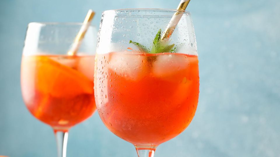 Zwei bauchige Gläser mit orangerotfarbenem Aperol Spritz mit Eiswürfeln und Orangenscheiben.