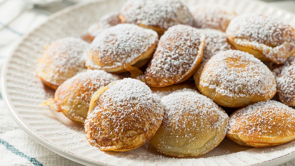 Holländische Poffertjes mit Puderzucker bestreut, angerichtet auf einem Teller